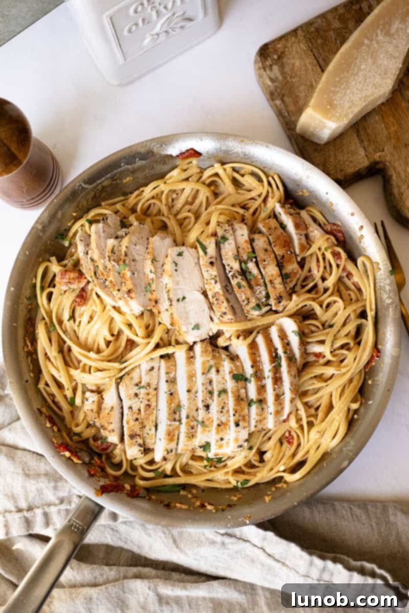 Creamy pasta in a pan topped with golden brown chicken, ready to serve.