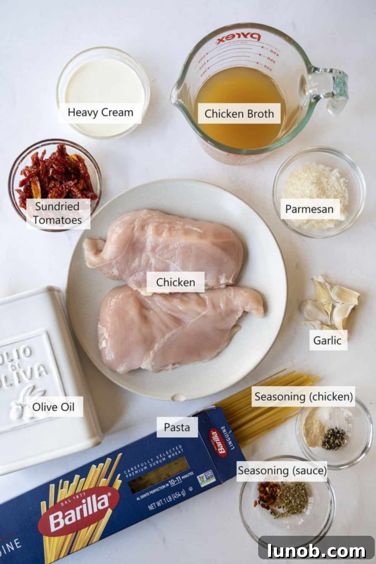 Fresh ingredients for creamy sundried tomato chicken pasta displayed on a wooden board.