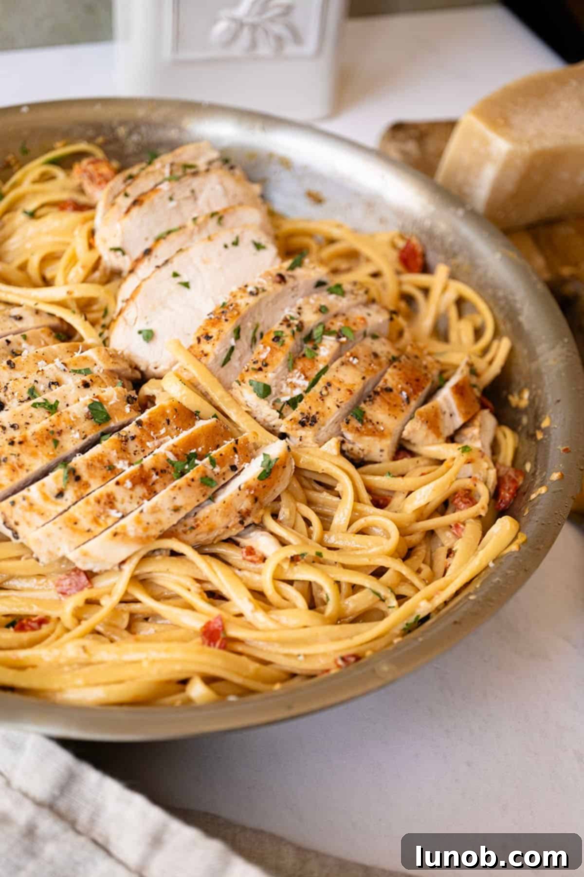 Close-up of creamy sundried tomato pasta garnished with fresh parsley and topped with sliced golden-brown chicken.