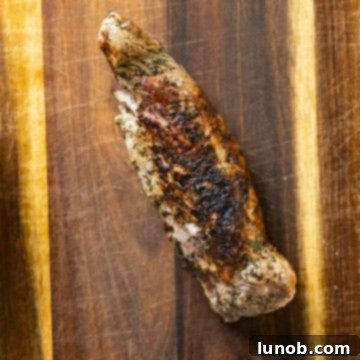 Rustic Italian Cast Iron Pork Tenderloin 7 Cooked pork tenderloin resting on a wooden cutting board after being removed from the pan.