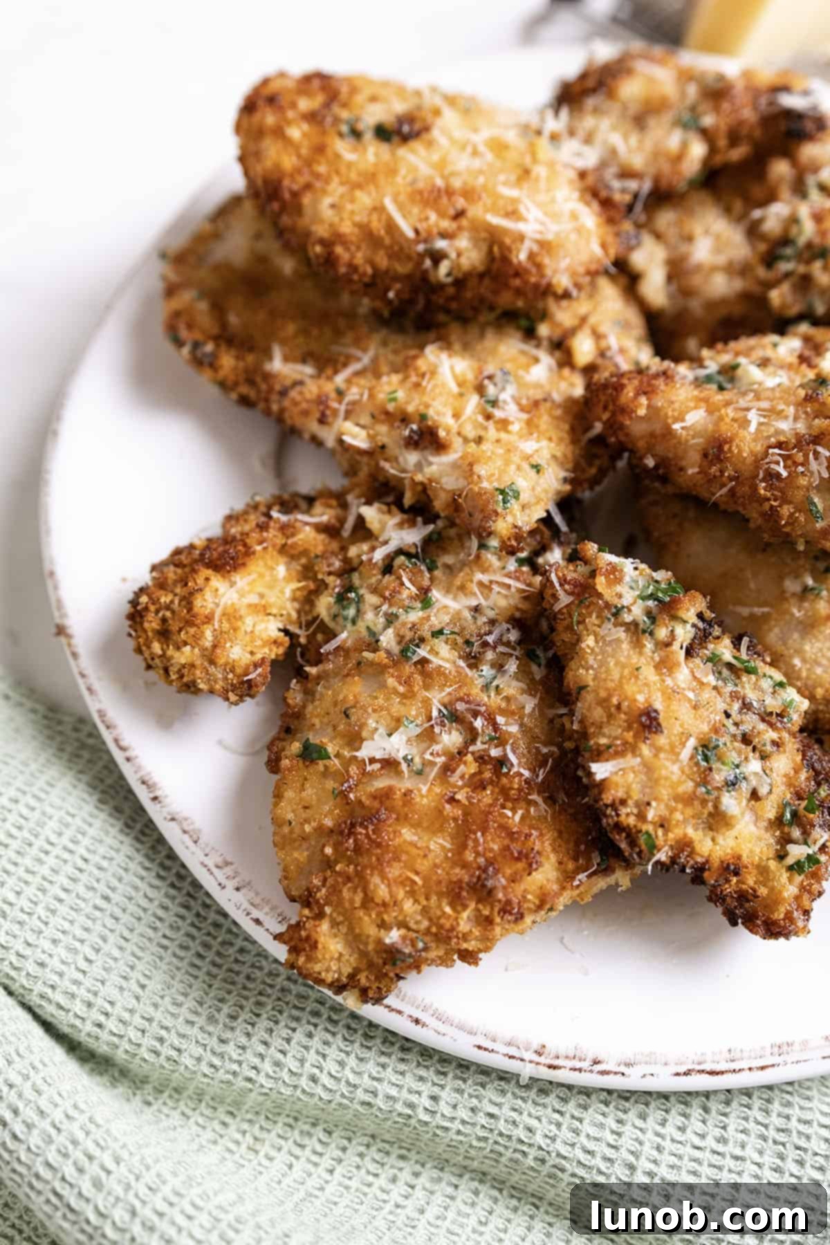 Golden-brown air fried chicken thighs coated in a rich garlic parmesan sauce, garnished with fresh herbs, ready to be served.