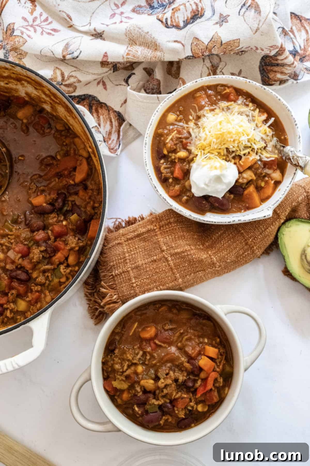 Golden Harvest White Bean Chili 13 Two bowls of white bean pumpkin chili, one topped with sour cream and cheese, next to a Dutch oven filled with chili, showcasing delicious serving options.