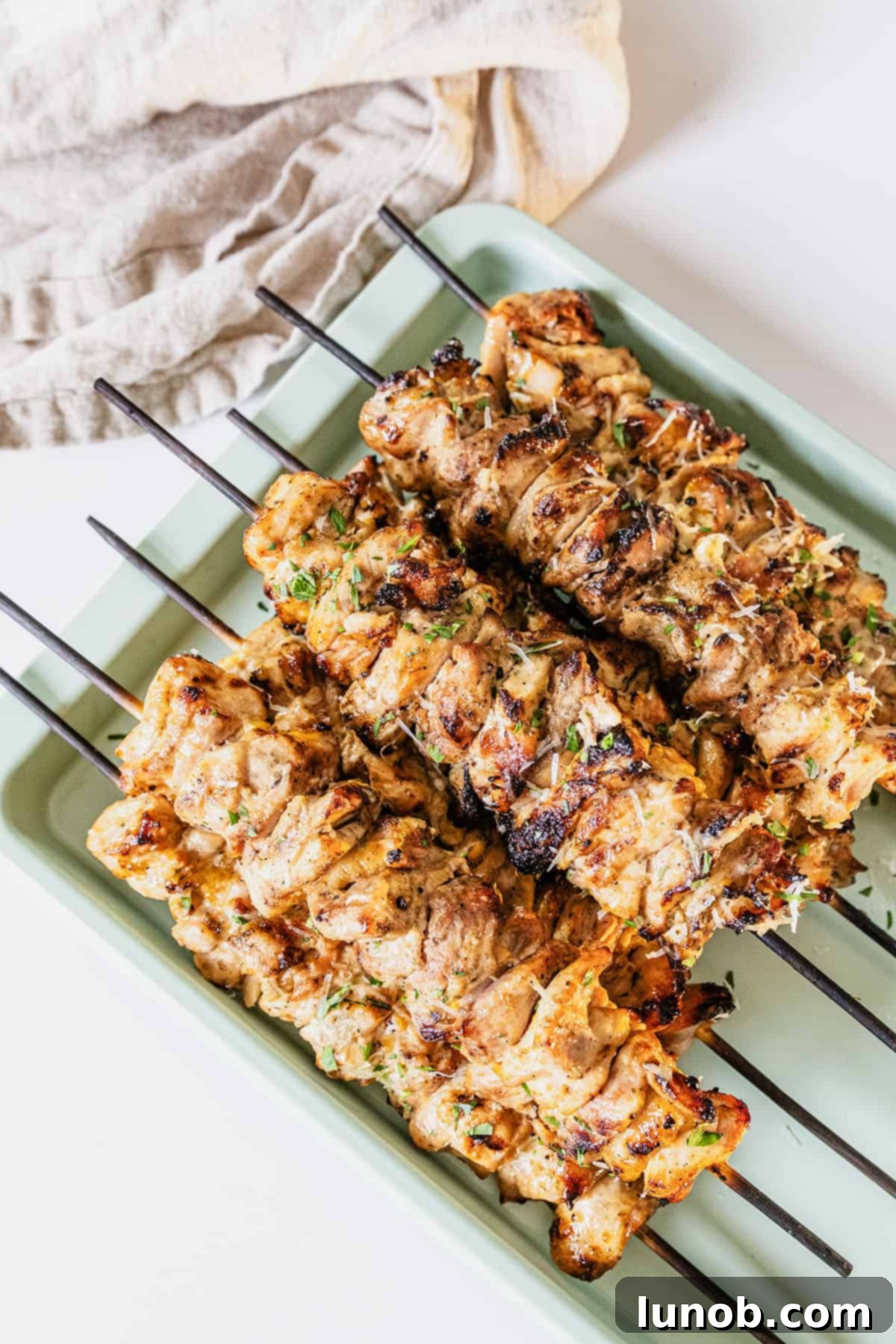 Savory Garlic Parmesan Chicken Skewers 2 Garlic parm chicken skewers on a baking pan basted with parm sauce.