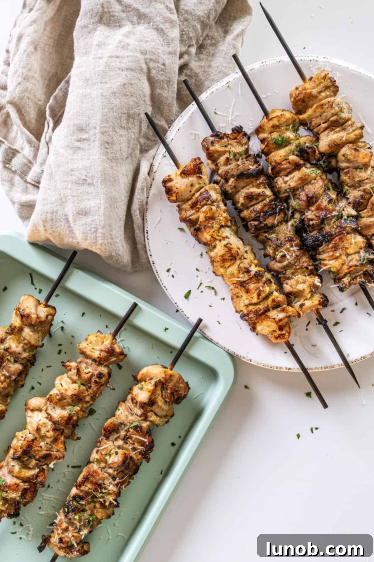 Savory Garlic Parmesan Chicken Skewers 11 Garlic parm chicken skewers on a plate basted with parm sauce.