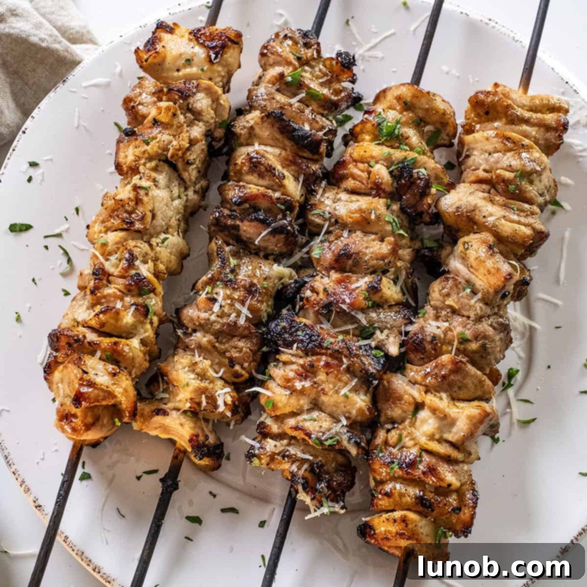 Savory Garlic Parmesan Chicken Skewers 10 Garlic parm chicken skewers on a plate basted with parm sauce.
