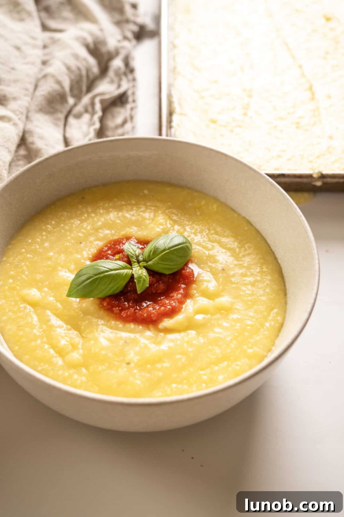 Velvety Golden Polenta 2 Creamy polenta in a bowl topped with marinara and basil.
