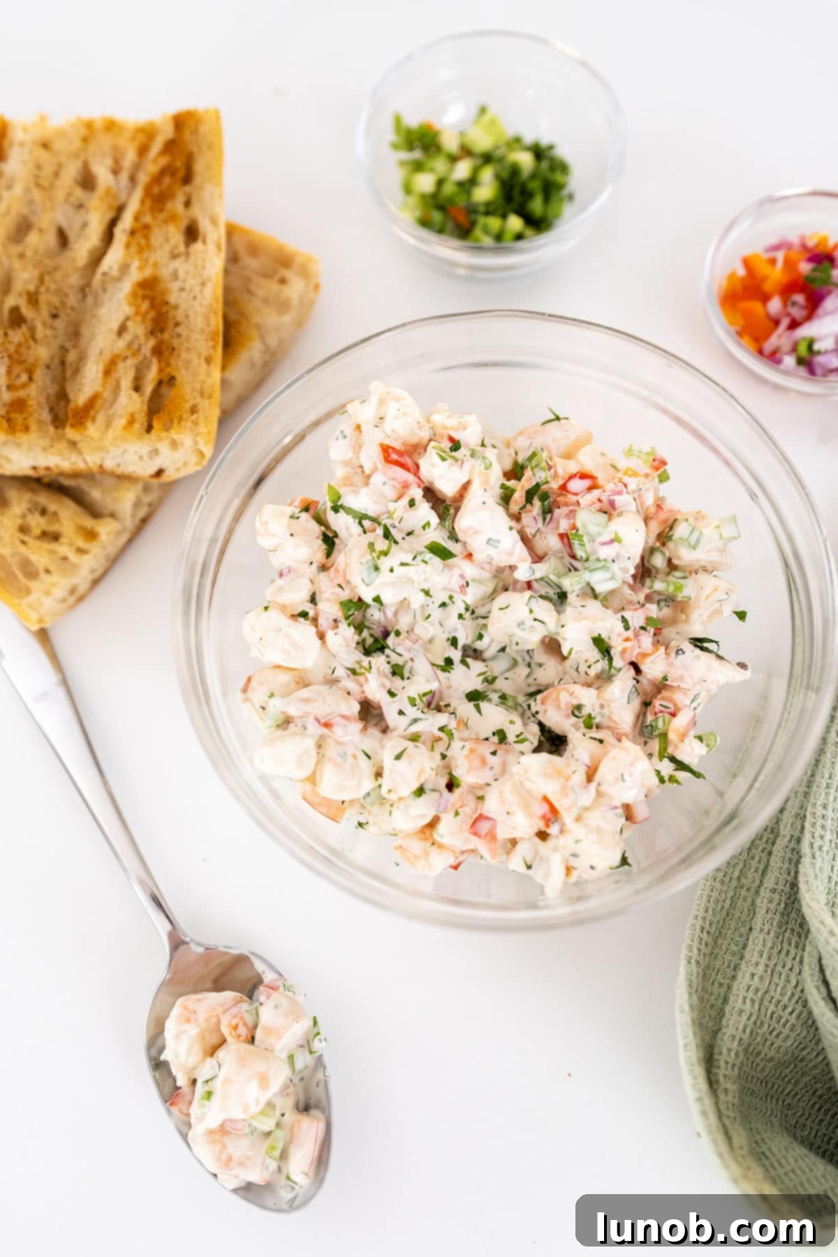 A vibrant bowl of cold shrimp salad, beautifully garnished, with a side of golden-brown toasted bread slices, ready for serving.