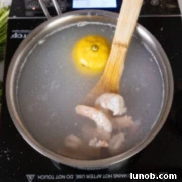 Shrimp being boiled in a pot of water with a slice of lemon to infuse flavor.