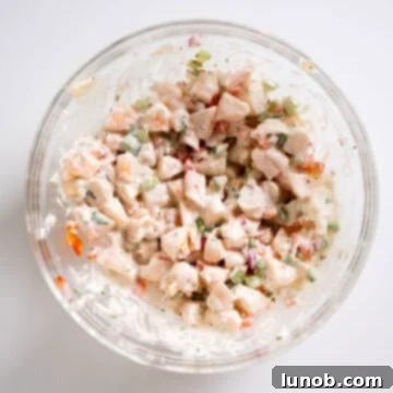 All the cold shrimp salad ingredients, including chopped shrimp, mayonnaise, and vegetables, thoroughly combined in a large bowl.