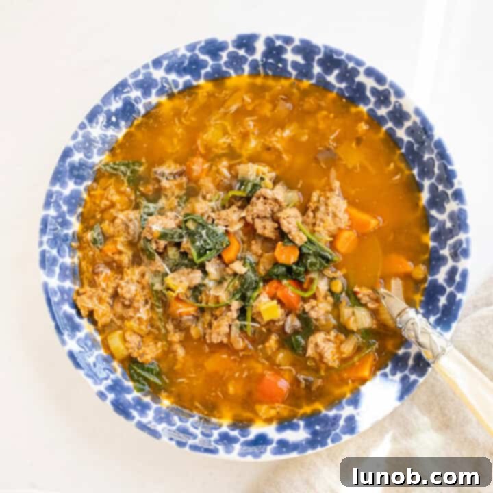 Hearty bowl of Italian sausage and lentil soup, garnished with fresh herbs.