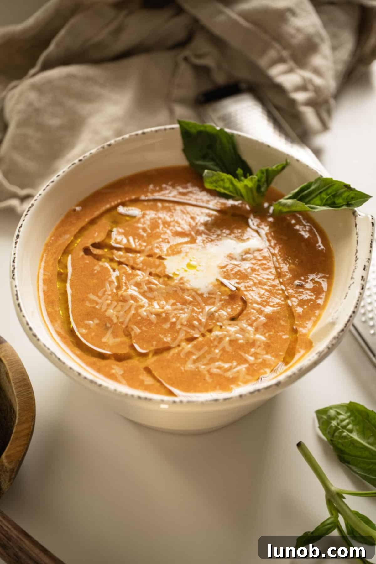 Rich Roasted Garlic and Tomato Cream Soup 2 A beautifully presented bowl of creamy roasted garlic and tomato soup, garnished with a swirl of cream, a drizzle of olive oil, and fresh basil leaves, ready to be enjoyed.