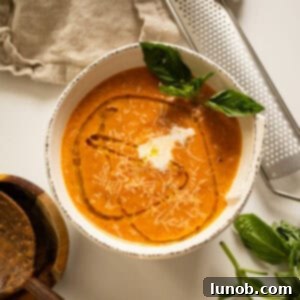Rich Roasted Garlic and Tomato Cream Soup 11 A beautifully presented bowl of creamy roasted garlic and tomato soup, garnished with a swirl of cream, a drizzle of olive oil, and fresh basil leaves.