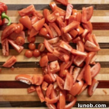 Rich Roasted Garlic and Tomato Cream Soup 5 A vibrant assortment of fresh tomatoes, including Roma, beefsteak, and cherry varieties, expertly chopped into uniform 1-2 inch pieces on a cutting board, ready for roasting.