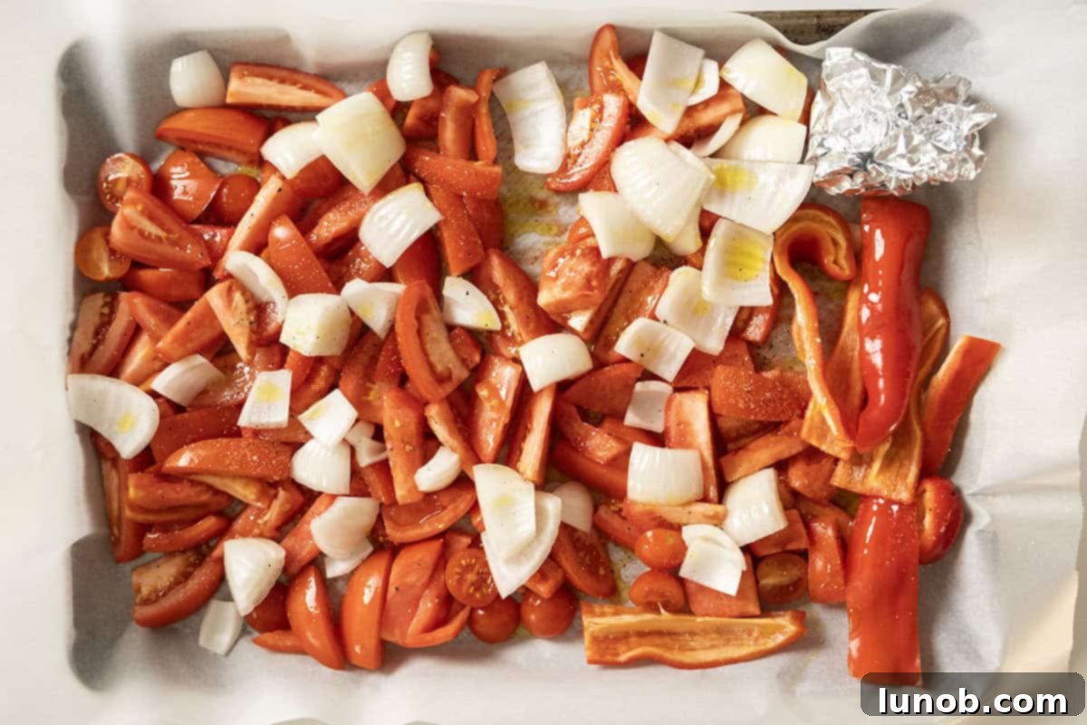 Rich Roasted Garlic and Tomato Cream Soup 6 A baking sheet lined with parchment paper, topped with chopped tomatoes, quartered onions, sliced red pepper, and the foil-wrapped head of garlic, all drizzled with olive oil and seasoned for roasting.