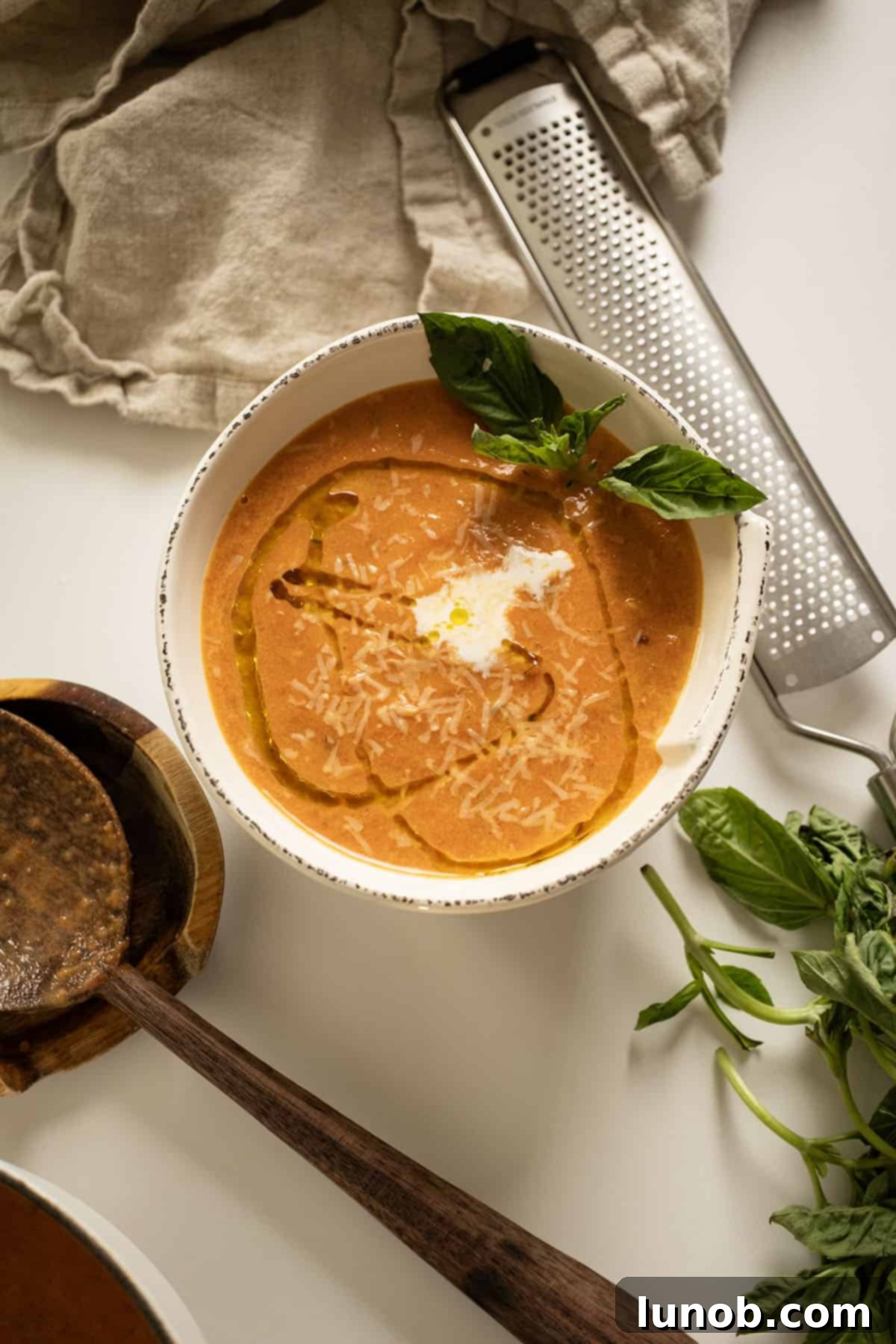Rich Roasted Garlic and Tomato Cream Soup 10 A close-up of a rustic bowl filled with rich, creamy tomato soup, elegantly garnished with a swirl of fresh cream, a few drops of vibrant olive oil, and delicate basil leaves, creating an inviting presentation.