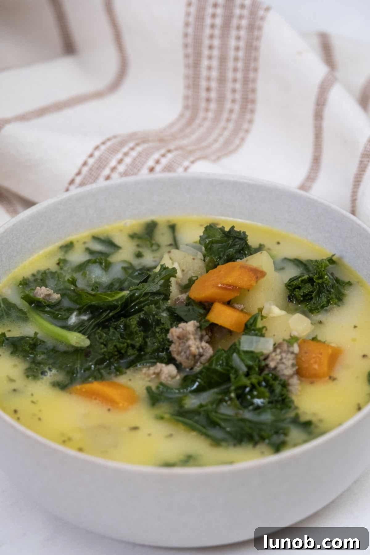 A bowl of Zuppa Toscana with carrots, potatoes, and sausage, garnished with fresh parsley.