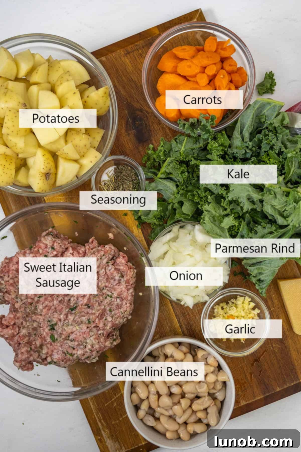 Fresh ingredients laid out for Zuppa Toscana, including sausage, potatoes, kale, carrots, onions, garlic, and herbs.