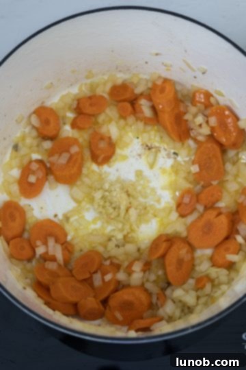 Sautéing a mixture of carrots, onions, and minced garlic in a Dutch oven.