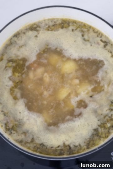 Zuppa Toscana soup simmering in a Dutch oven, with potatoes and vegetables visible.