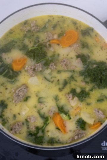Heavy cream being stirred into the finished Zuppa Toscana soup, making it creamy.