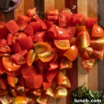 Freshly chopped ripe tomatoes on a wooden cutting board, diced into bite-sized pieces.