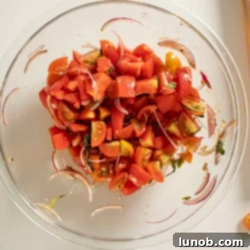 A large bowl showing chopped tomatoes, thinly sliced red onion, and fresh basil, mixed with olive oil and balsamic vinegar.