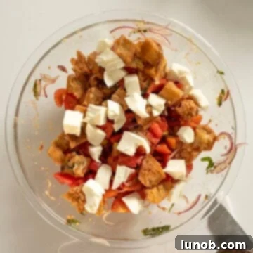 Fresh mozzarella pieces being gently tossed into the Panzanella salad, alongside the bread and vegetable mixture.