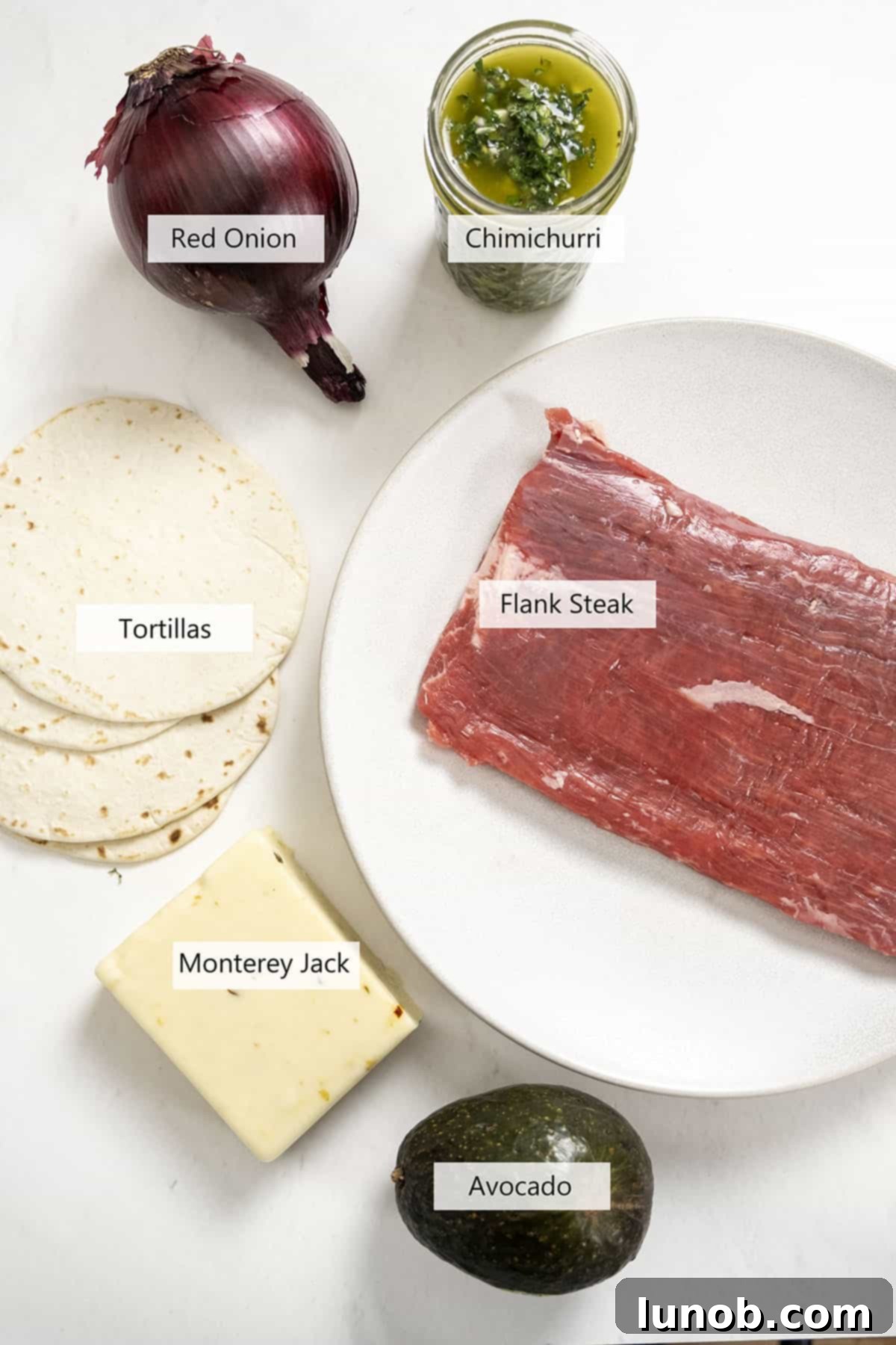 Vibrant Chimichurri Steak Tacos 4 Ingredients for assembling chimichurri steak tacos, including flank steak, tortillas, red onion, avocado, and cheese.