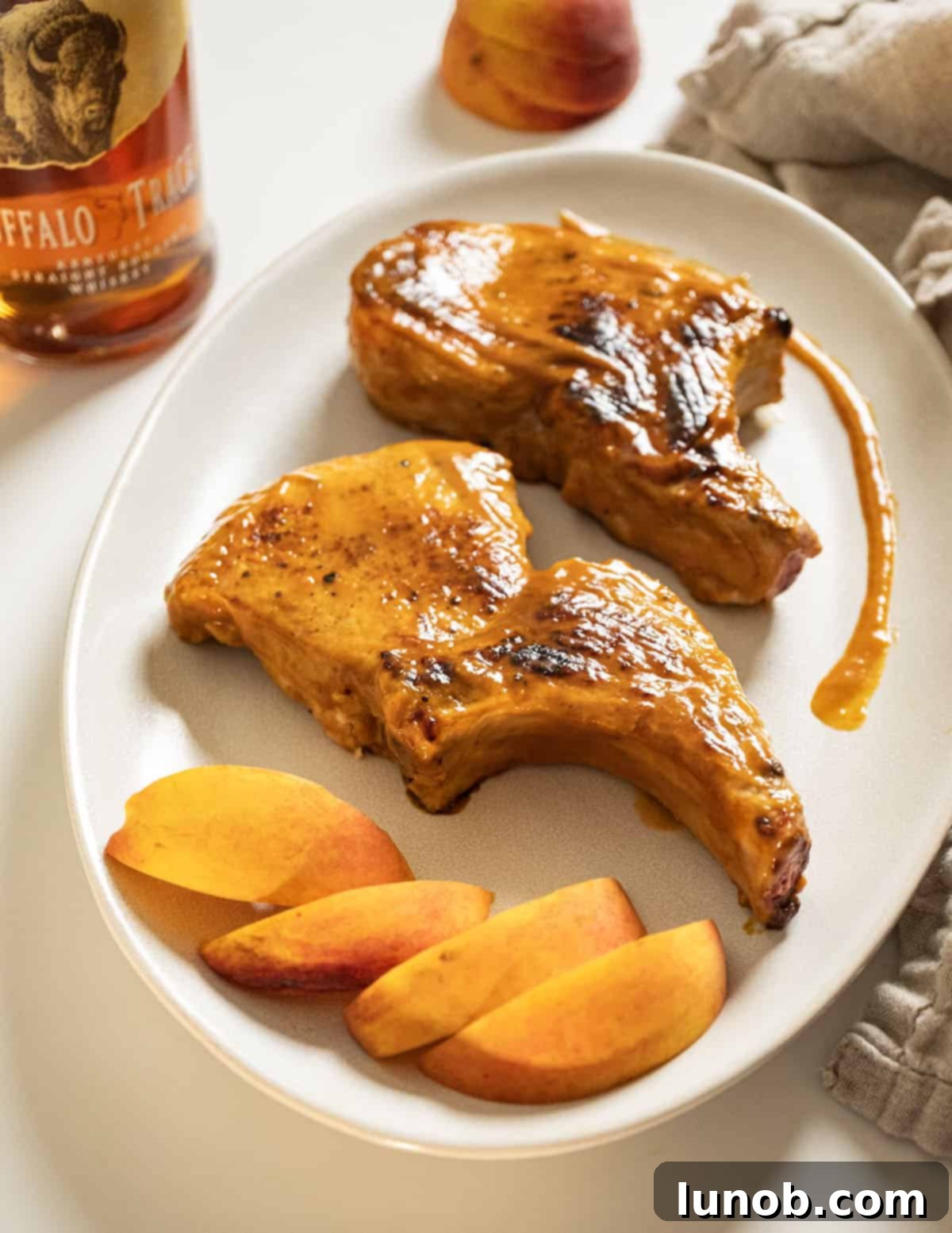 Perfectly cooked bourbon peach glazed pork chops on a white plate, garnished with fresh peach slices and a drizzle of extra sauce.