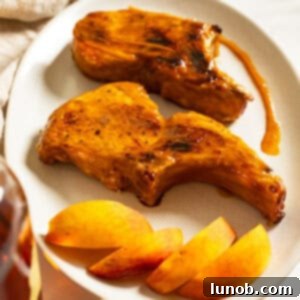 Bourbon peach glazed pork chops on a plate garnished with peaches and extra sauce.