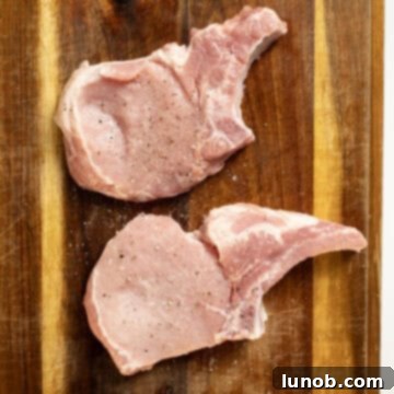 Bone-in pork chops generously seasoned with salt and freshly ground black pepper, ready for cooking.