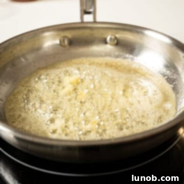 Fresh garlic being sautéed in melted butter in a small saucepan, releasing its aromatic fragrance.