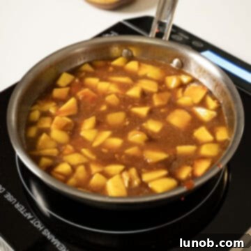 Chopped fresh peaches simmering in a rich, bubbling sauce within a saucepan, absorbing all the flavors.