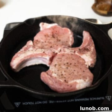 Seasoned pork chops searing in a hot cast iron skillet, developing a golden-brown crust.