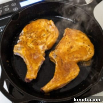 Pork chops being glazed with the sticky bourbon peach sauce in a cast iron skillet, caramelizing beautifully.