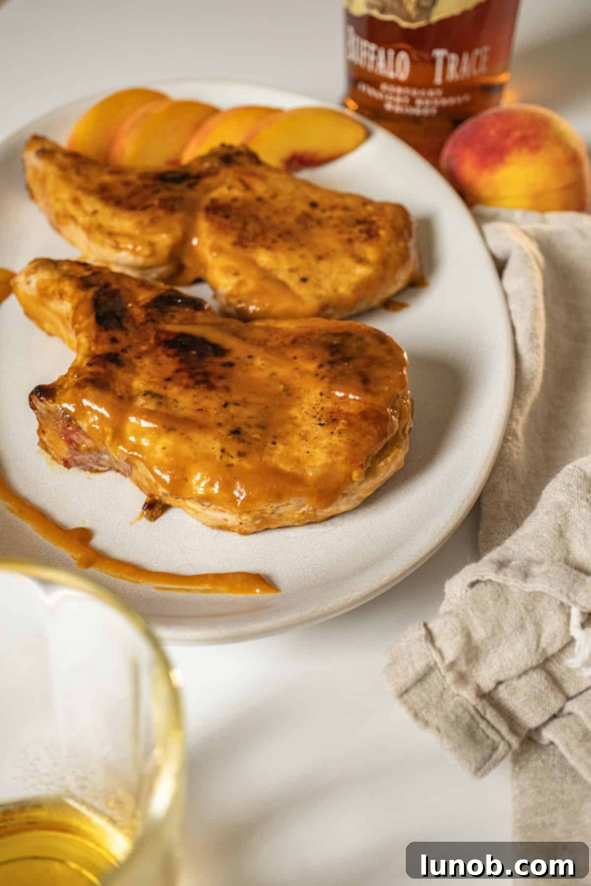 Close-up of bourbon peach glazed pork chops on a plate, glistening with sauce and garnished with fresh peach slices.