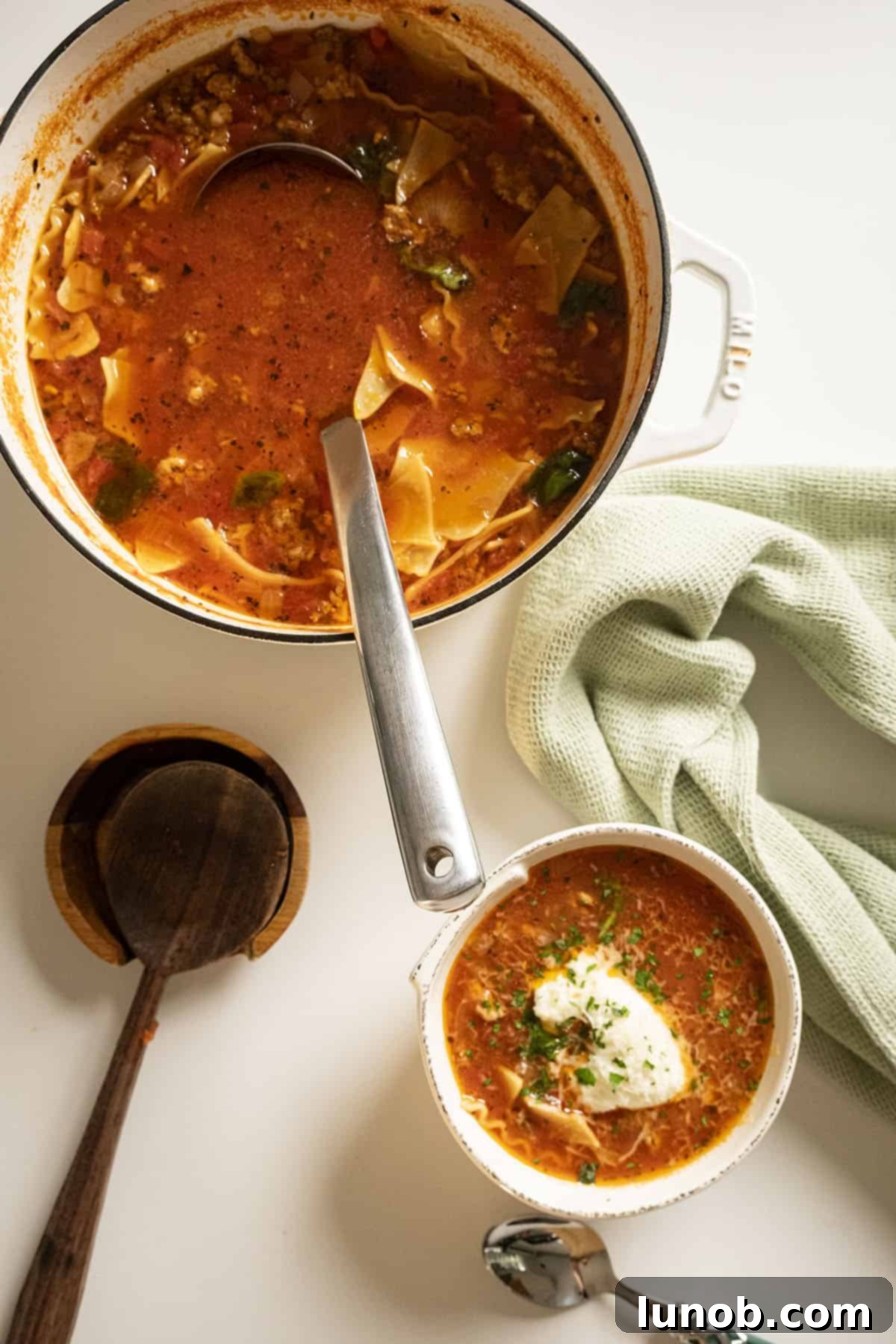 Ultimate One-Pot Lasagna Soup 12 A large pot of simmering lasagna soup beside a serving bowl garnished with ricotta, parsley, and parmesan.