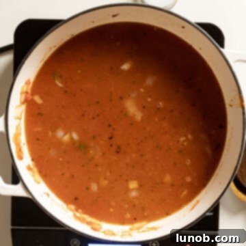Ultimate One-Pot Lasagna Soup 9 Golden chicken broth being poured into the pot with marinara and meat, along with a parmesan rind, ready to simmer and infuse flavor.