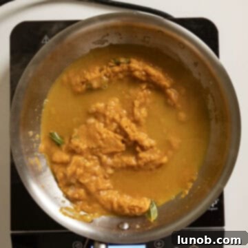 Velvety Pumpkin Pasta 8 Pumpkin puree being mixed into the shallot and sage infused brown butter in a pan, with pasta water being added to create the sauce.