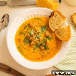 Butternut squash soup with sausage in a bowl and side of crusty Italian bread.