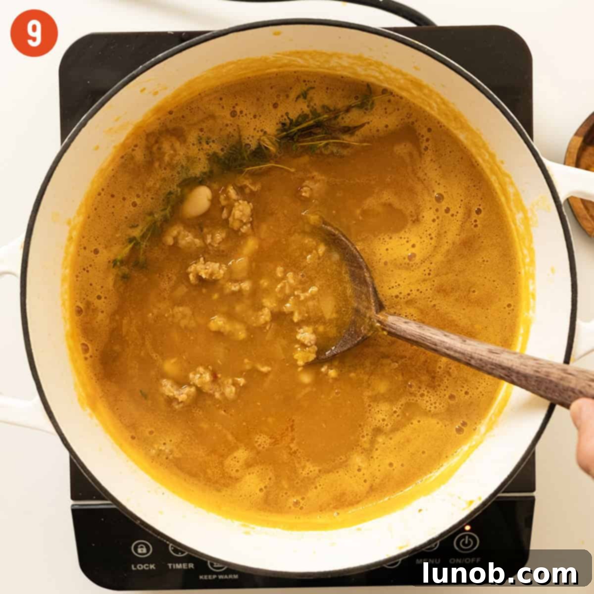 Butternut squash soup simmering gently in a Dutch oven with cannellini beans and browned Italian sausage returned to the pot.
