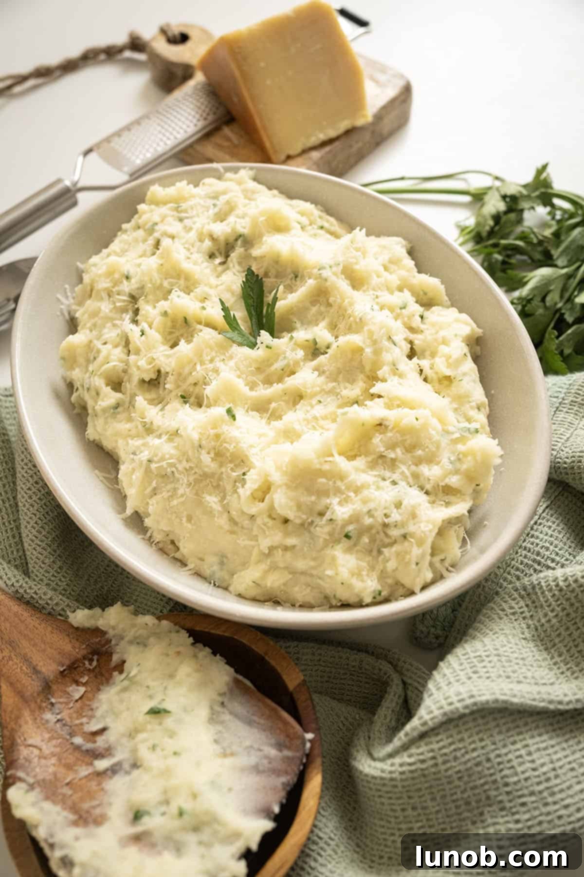 Garlic parmesan mashed potatoes in a bowl, garnished with fresh parsley.
