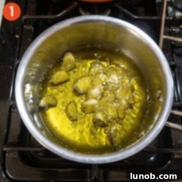 Garlic cloves gently simmering in a pot of olive oil over low heat.