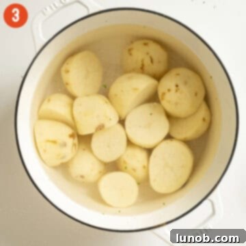 Halved and peeled Russet potatoes in a large pot, ready for boiling.