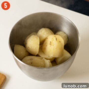 Hot, boiled potatoes in the bowl of a stand mixer, partially mashed.