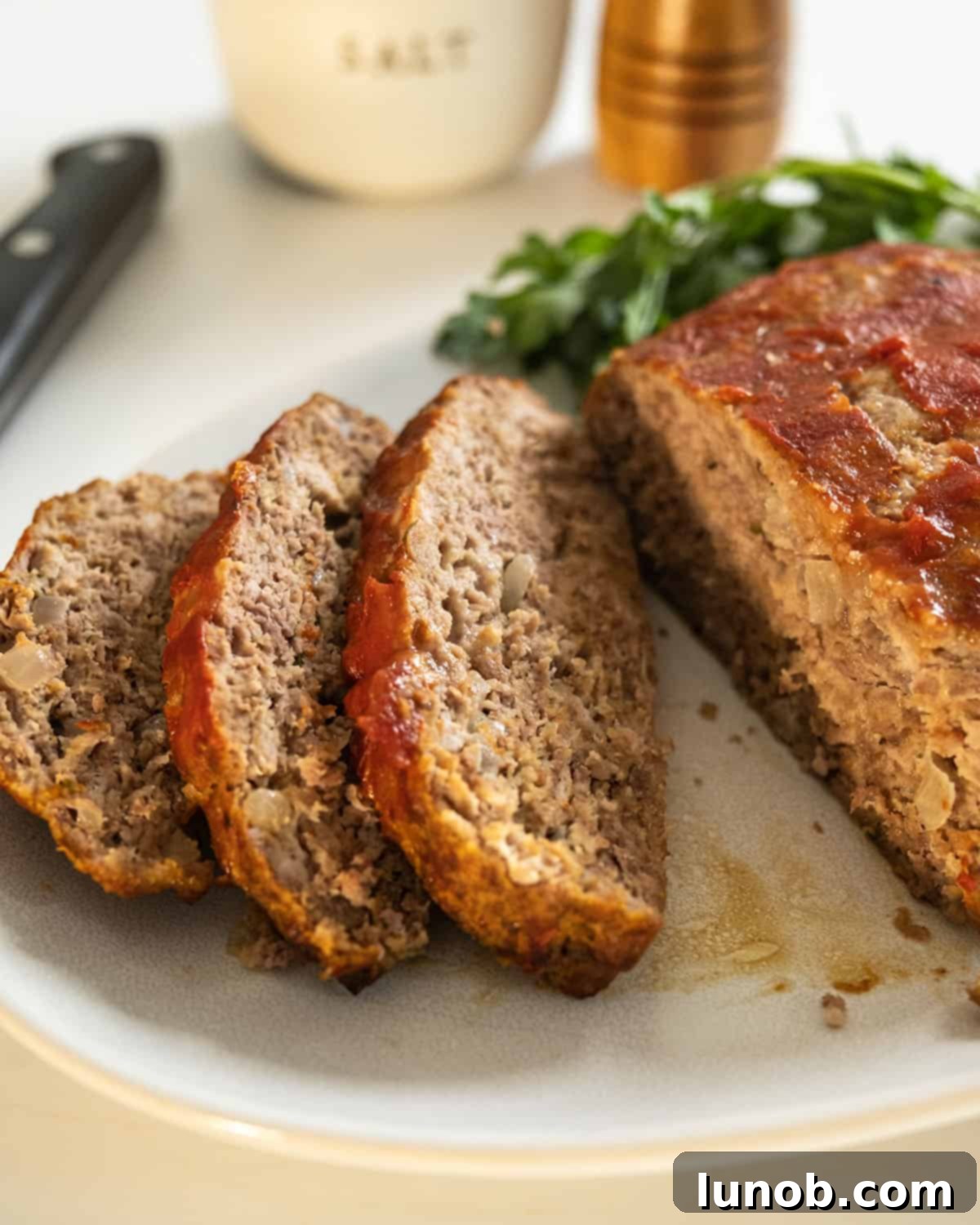 Slices of tender Italian meatloaf, rich with herbs and cheese, served on a white plate alongside vibrant marinara sauce.