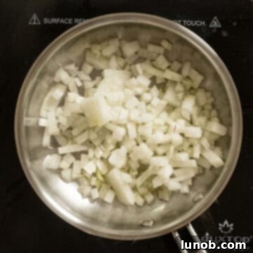 Finely diced onions being sautéed in a pan with olive oil until softened and lightly browned.