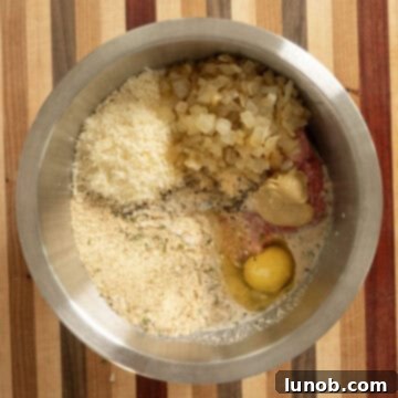 A large mixing bowl containing all the raw ingredients for Italian meatloaf: meat, breadcrumbs, cheese, milk, and spices.