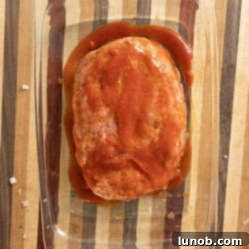 Italian meatloaf covered generously with marinara sauce in a baking dish, prepared for the oven.