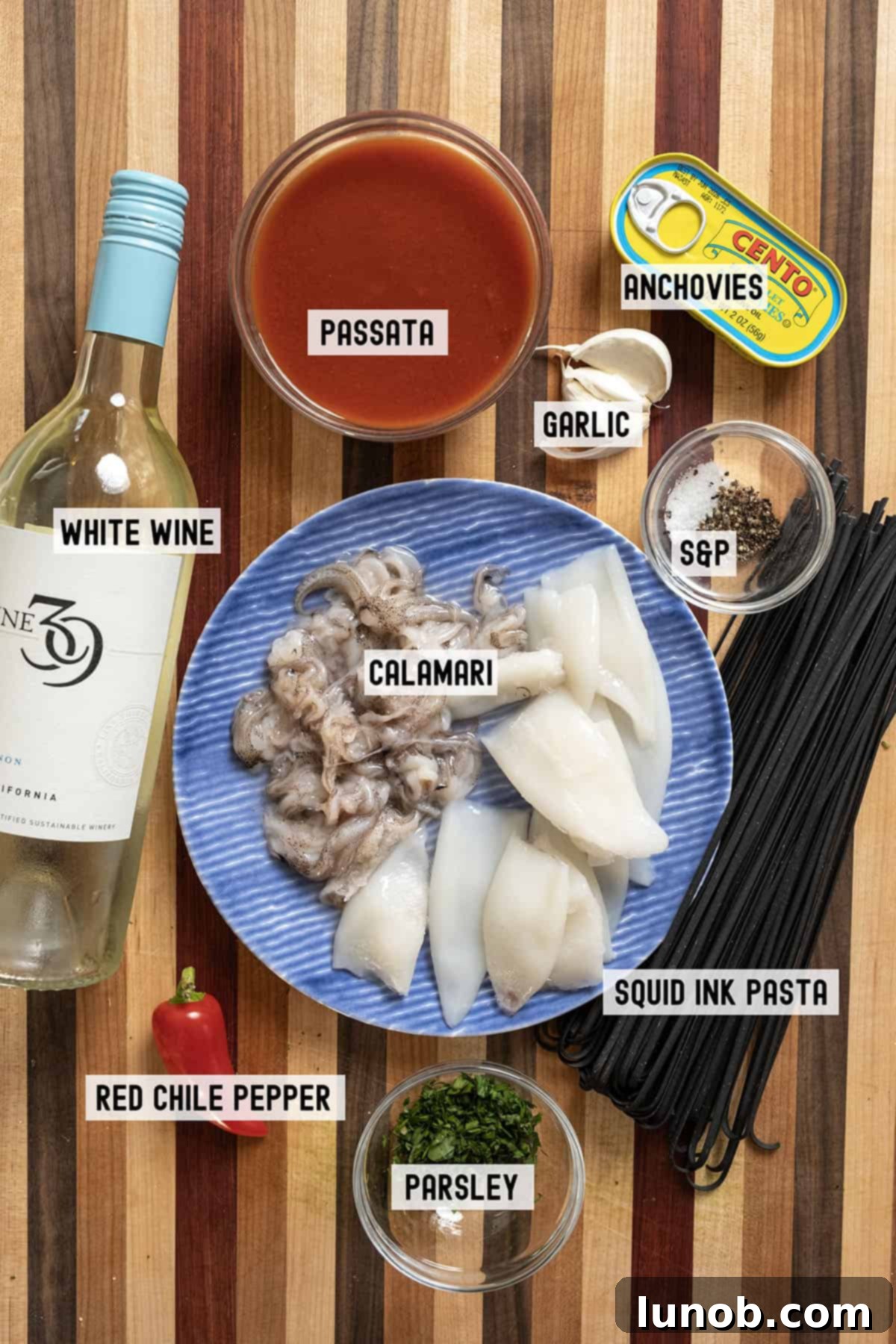 Ebony Ocean Pasta with Seared Calamari 3 Fresh ingredients laid out on a wooden board, including calamari, garlic, chili, wine, and passata for pasta.